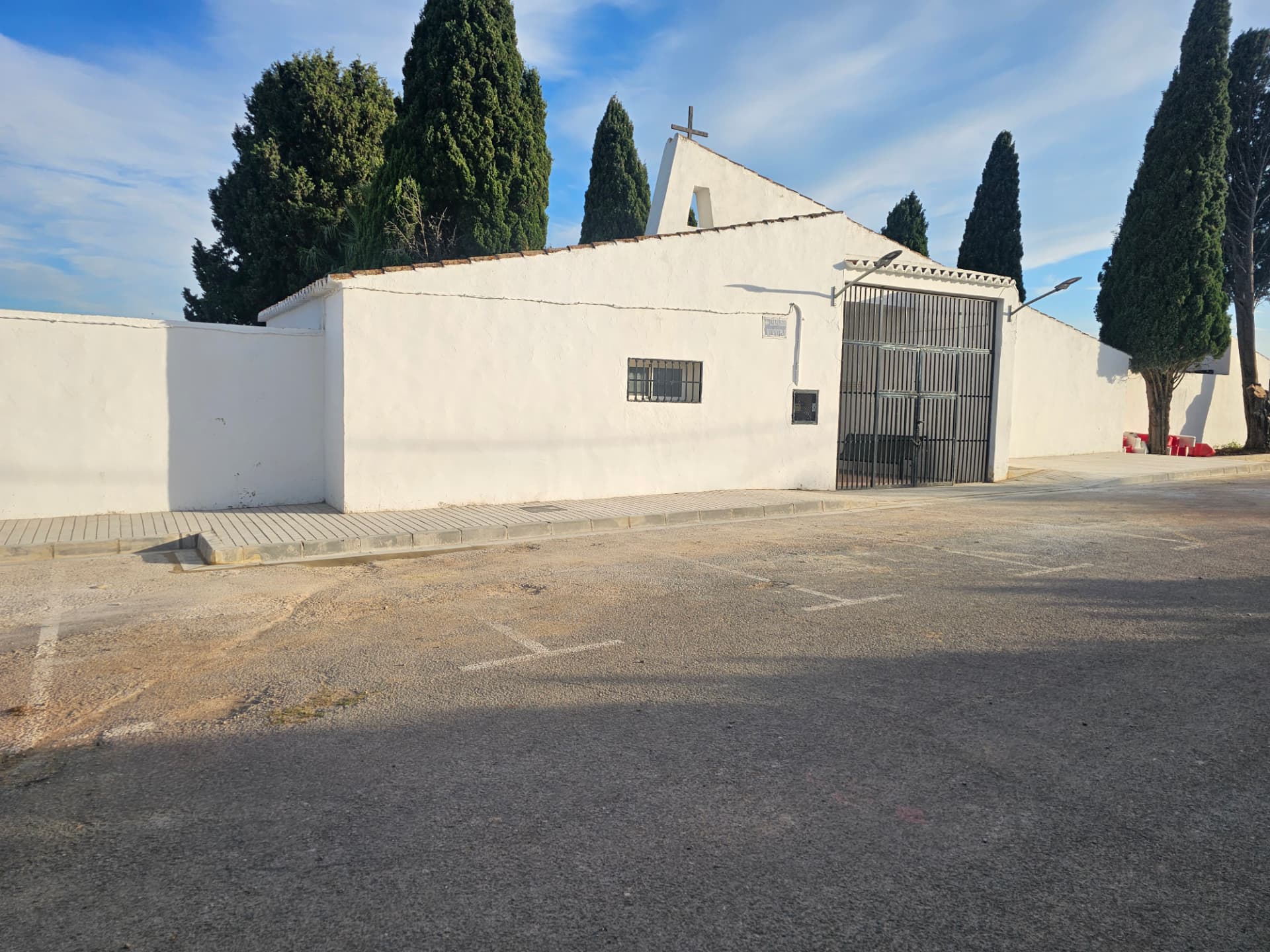 Fachada del cementerio con la acera y la zona de aparcamiento