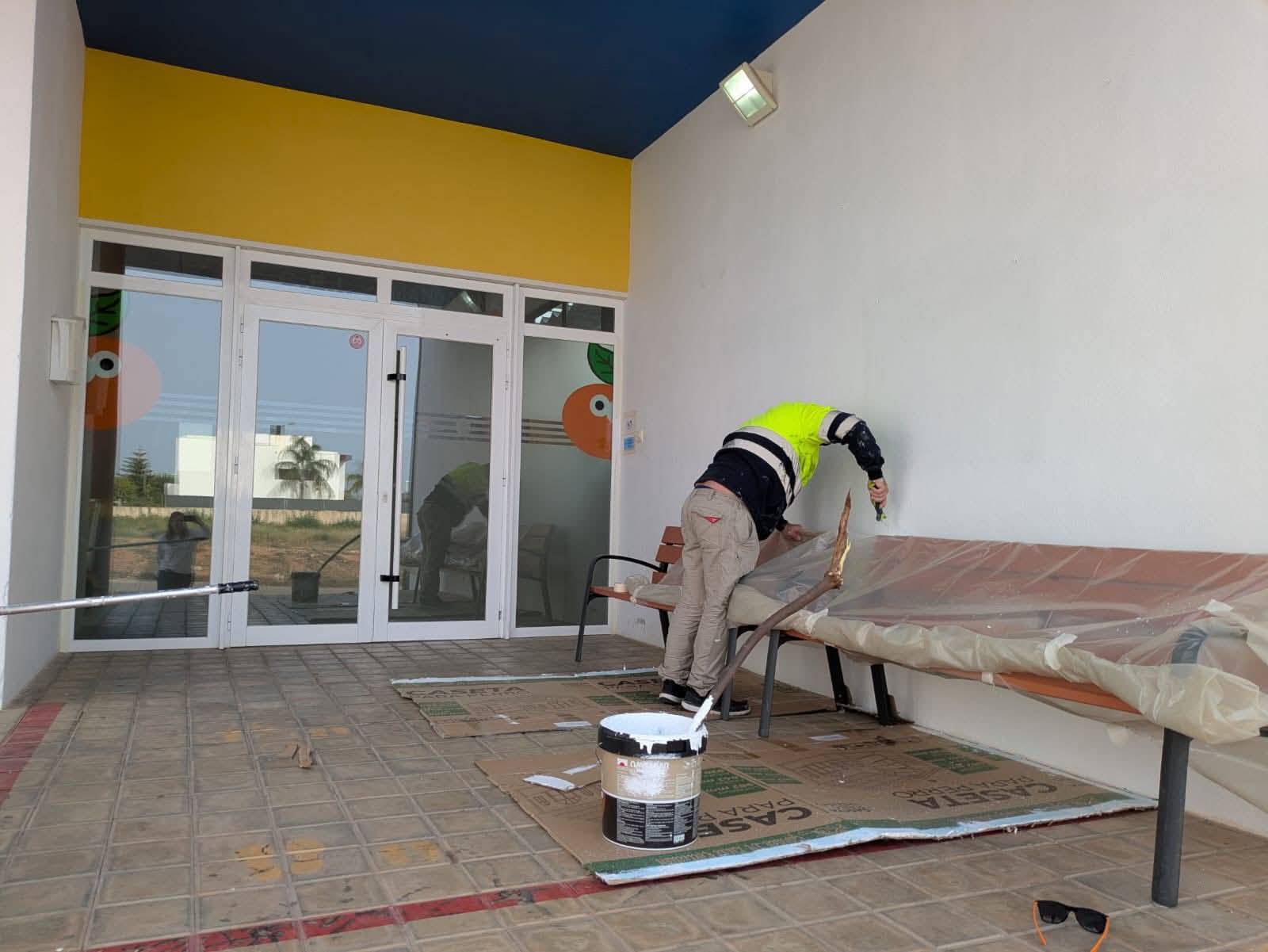 Operario municipal pintando la pared exterior de un edificio público.